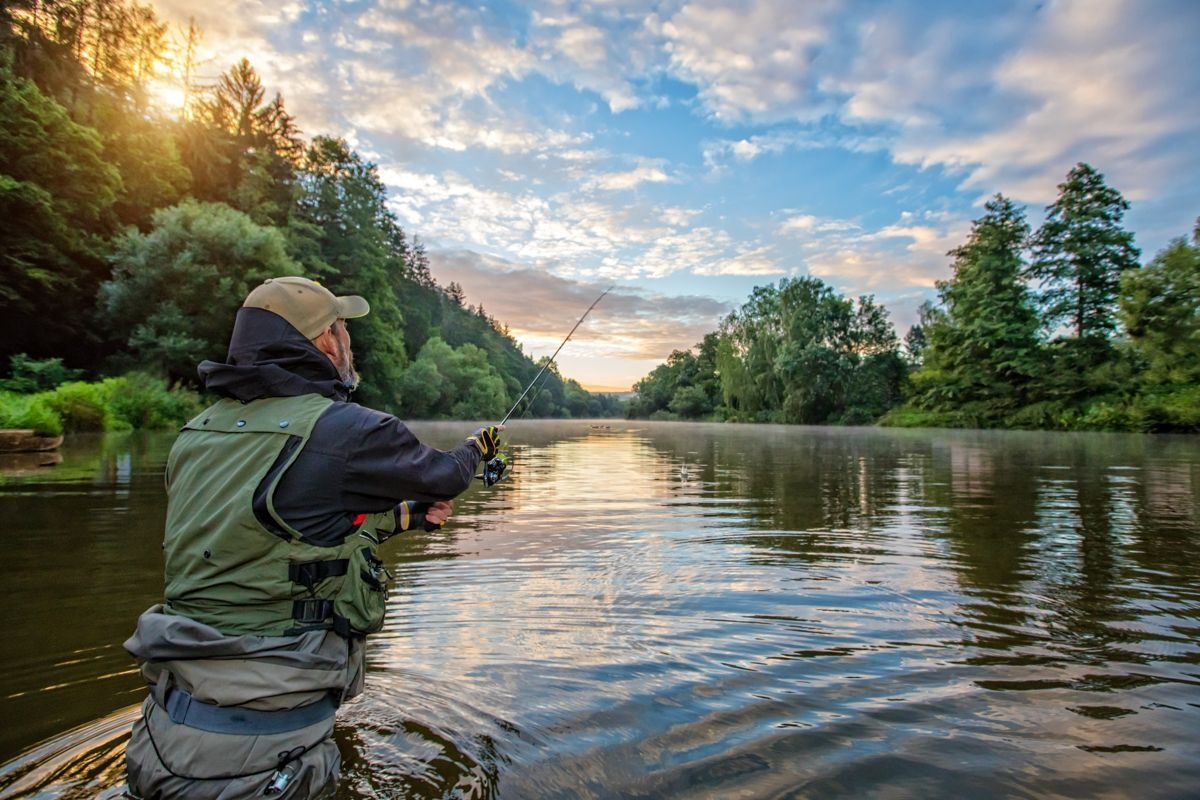 Wędkarz nad jeziorem z wędką o wschodzie słońca – pokrowce wędkarskie i outdoorowe szyte na miarę.